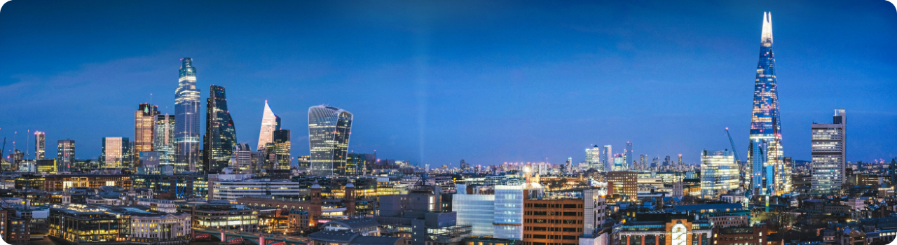London's financial district skyline lit up at dusk, viewed across the city rooftops.