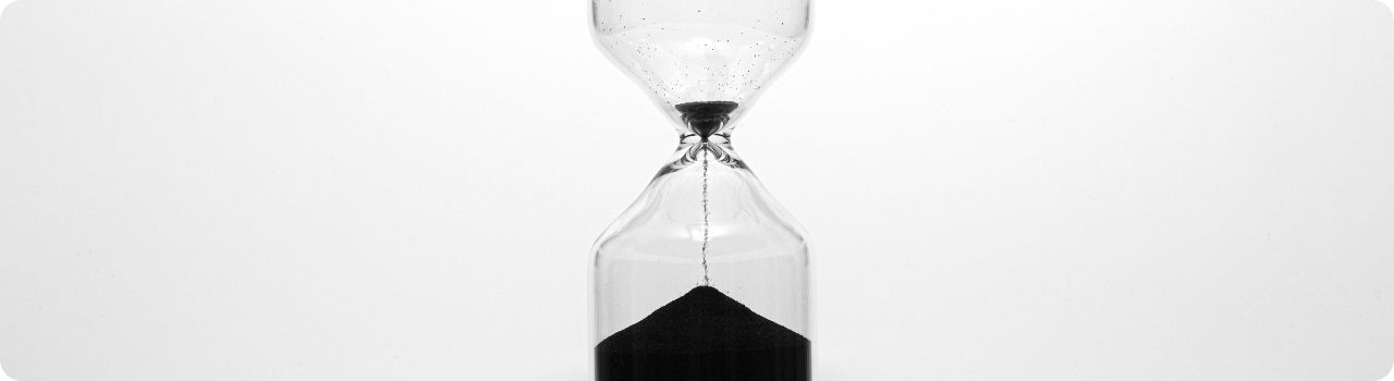 Black-and-white hourglass with the top bulb almost empty and the last thin stream of sand falling onto a pile below.
