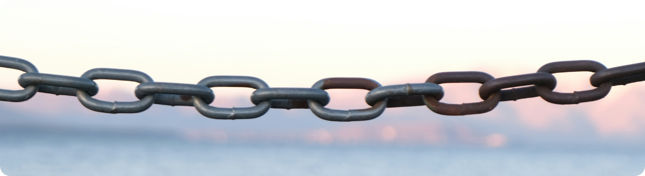 A steel chain stretched across a hazy pink sky, its links turning from grey to rust towards the right, illustrating an investment only as strong as its weakest part.