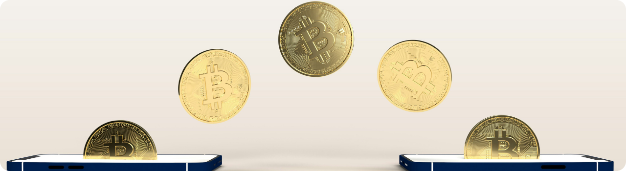 Gold bitcoin coins passing in an arc from one smartphone to another against a beige background.