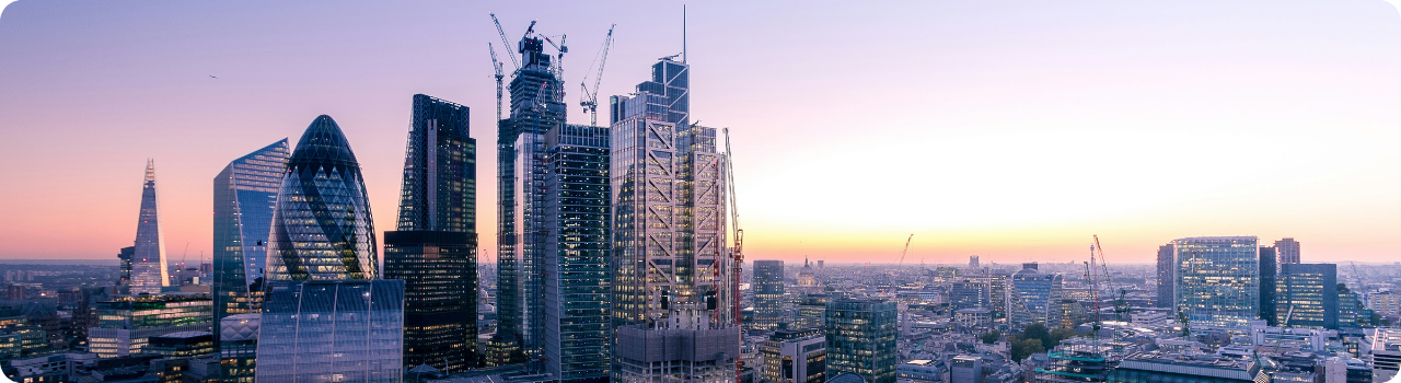 Alt text: London skyline at sunset, with the Shard, the Gherkin and the Leadenhall Building rising above the City under a purple and orange sky.